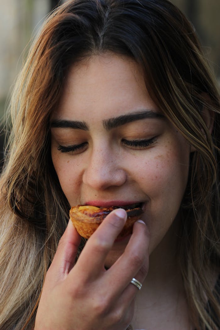 Close-up of a woman savoring a pastel de nata in Porto, showcasing local cuisine.