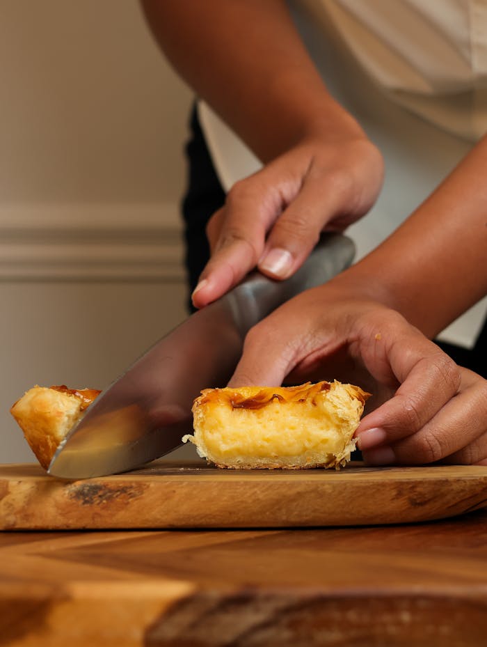 Close-up of hands slicing a Portuguese pasteis de nata on a wooden board.